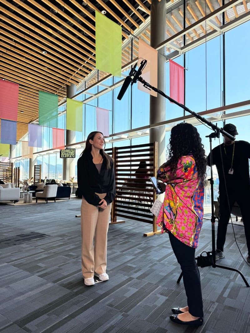 Ania Wysocka being filmed for an on-camera interview in a bright conference venue lobby with colorful hanging banners